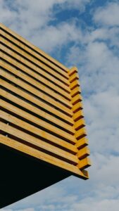 Een moderne houten structuur met een geometrisch ontwerp contrasteert met een heldere blauwe lucht op de achtergrond.